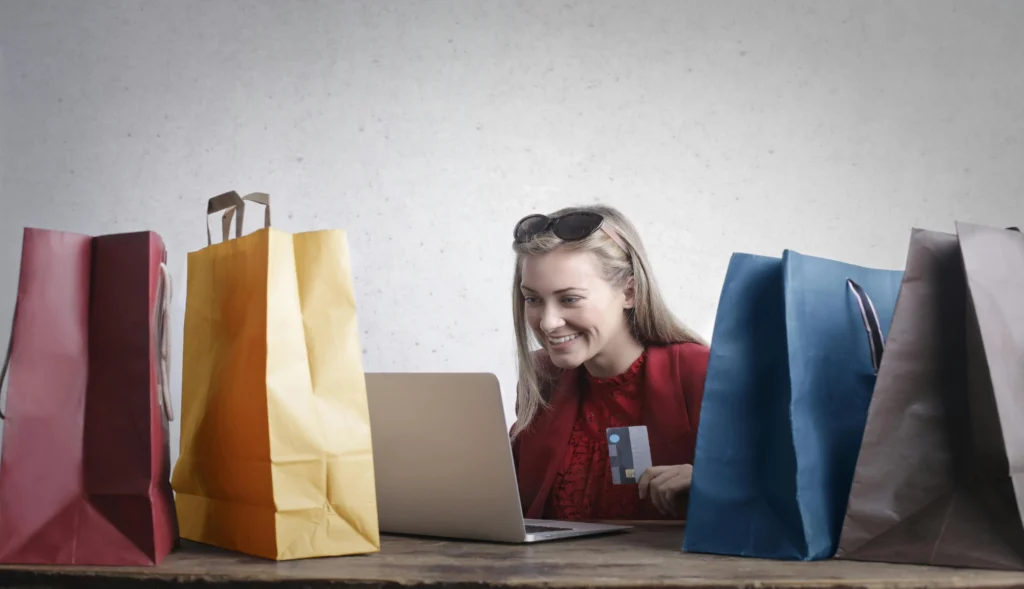 An image of a woman sitting on a desk with shopping bags preparing to purchase online